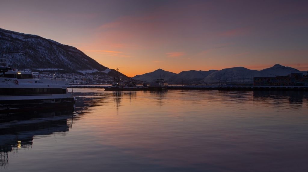 Norwegian_landscape_featuring_ the_glow_of_a_sunset_over_a_serene_fjord_framed_by_mountain_silhouetted_against_the_colorful_sky