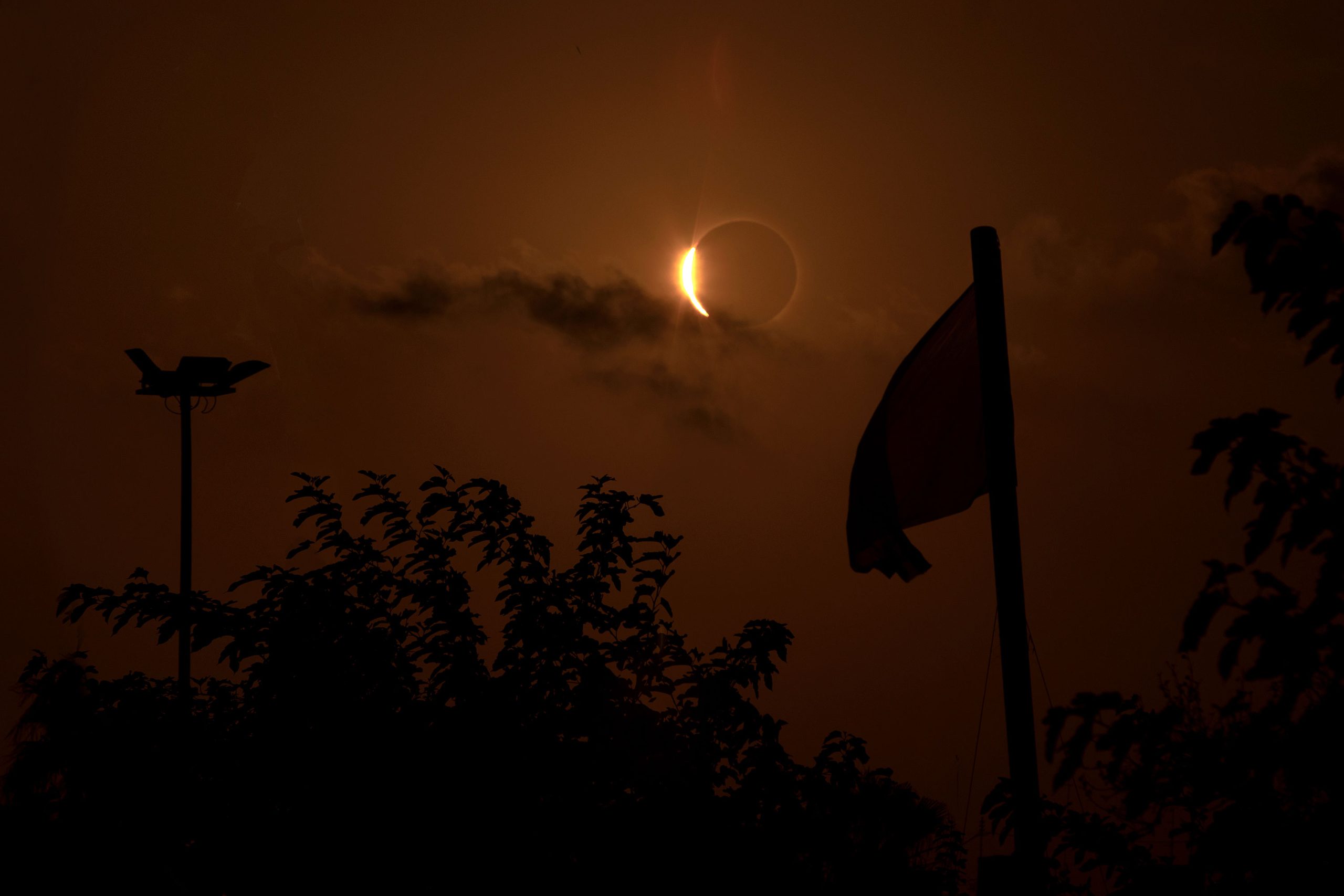 seconds_before_total_solar_eclipse_above_silhouetted_trees_and_a_flag